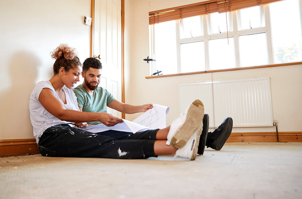 couple-sitting-on-floor-looking-at-plans-in-empty