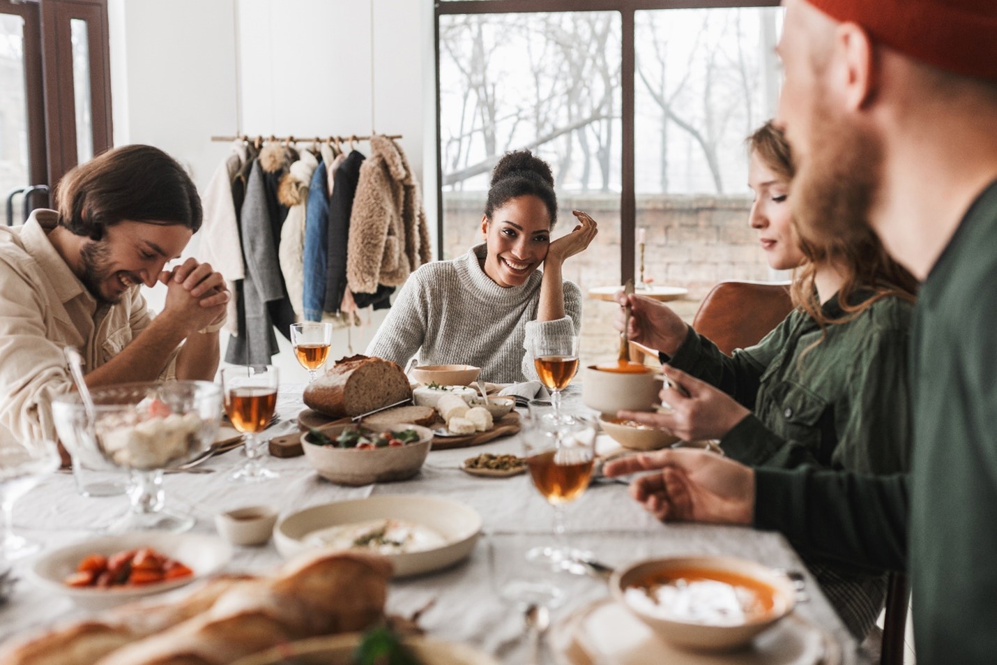 A group of four people gathered in front of a meal. They are wearing sweaters and flannels and appear happily smiling.