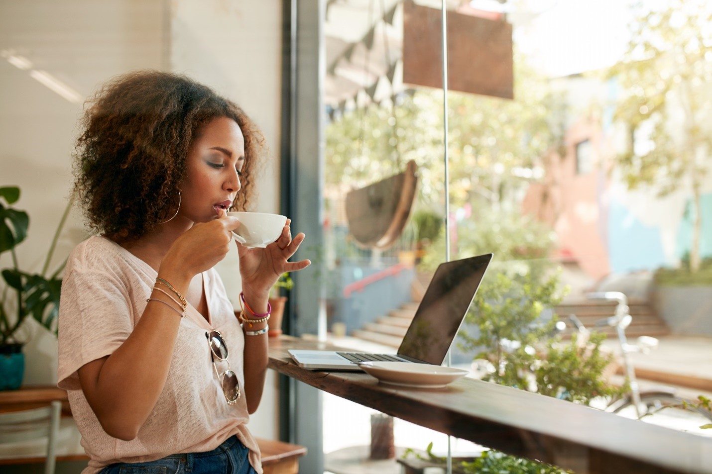 A young woman sitting in a cafe in front of a laptop, about to sip a coffee.