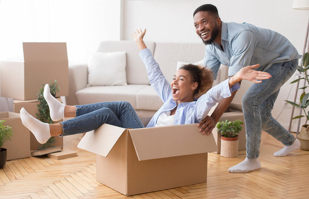 excited-man-riding-woman-in-moving-box-in-new-hous