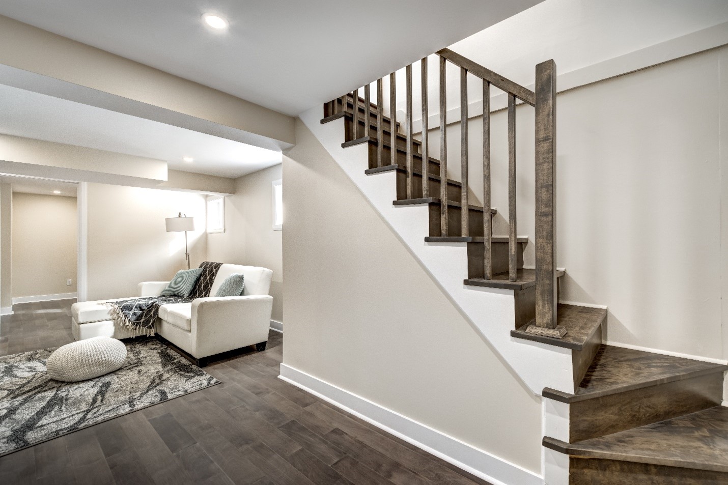 A furnished basement with beige walls, dark wood flooring, and a couch decorated with a blanket and pillows.