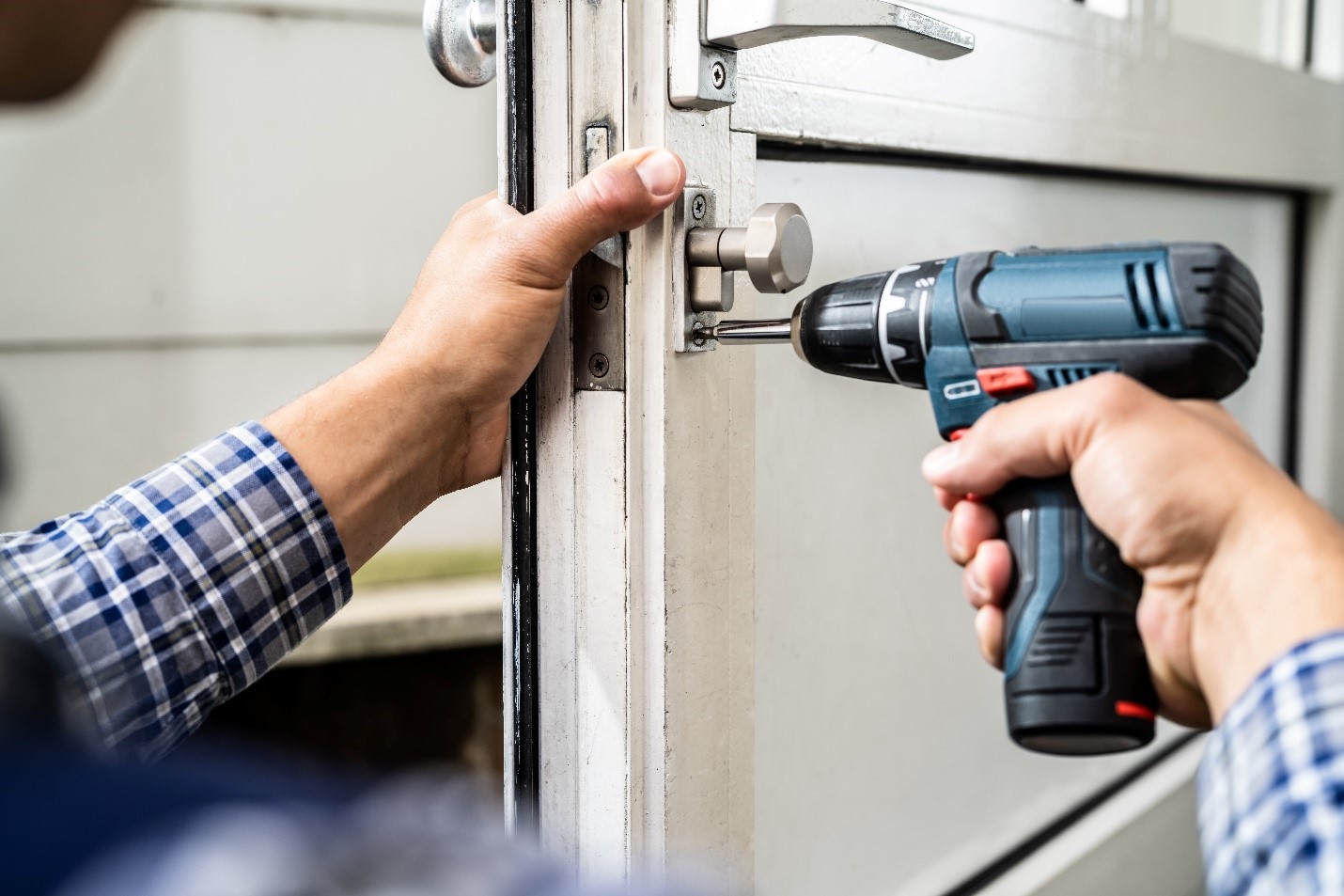 A close up image of a person with a drill working on a lock in a door.