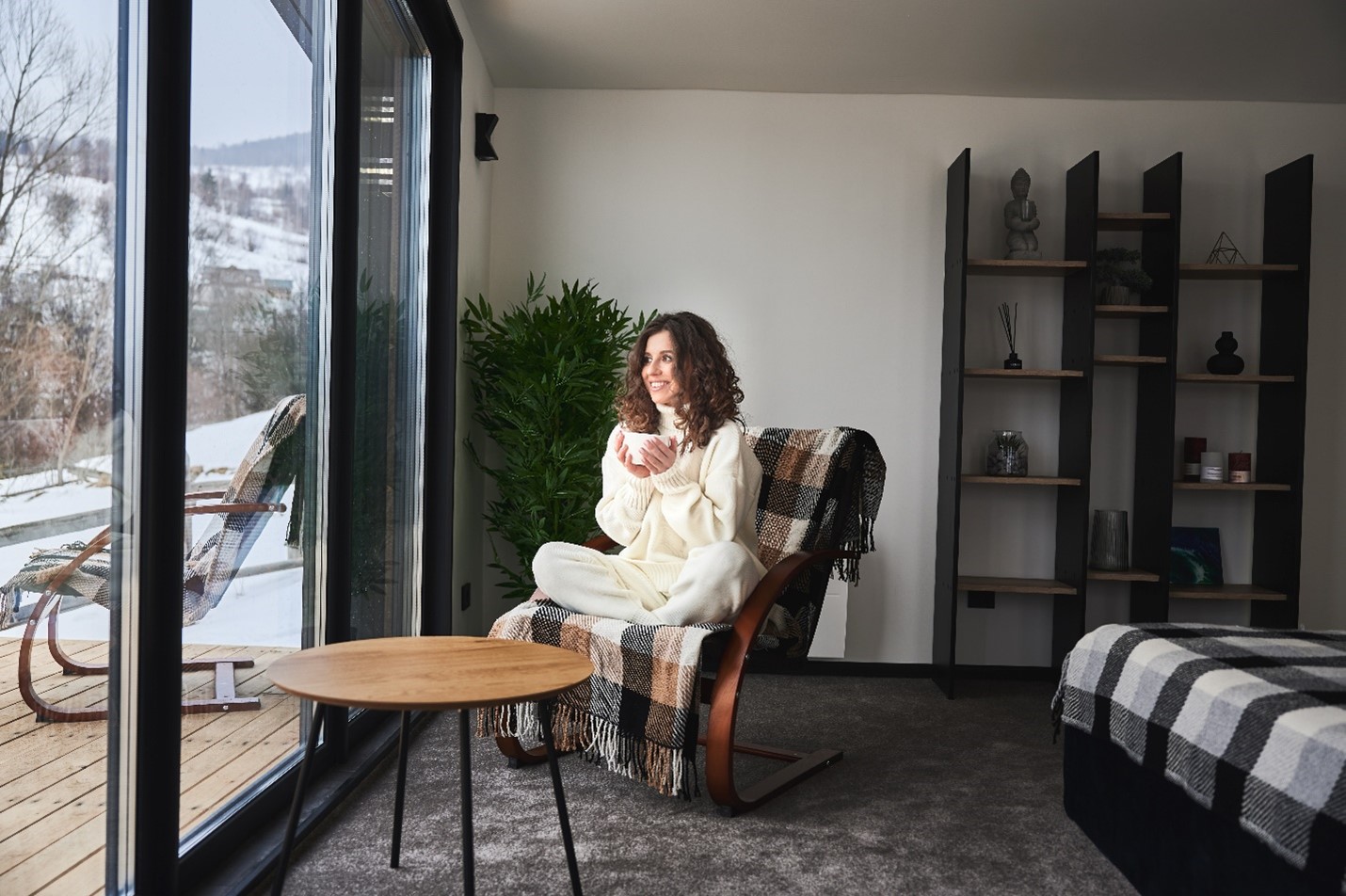 A woman happily holding a drink as she looks out at her snow covered lawn.