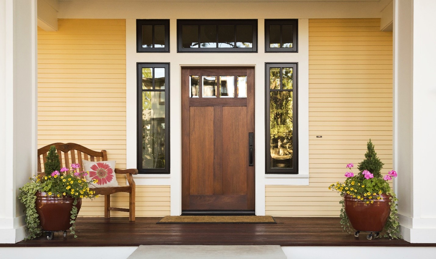 A front door exterior with two matching planters and a clean wooden deck floor.