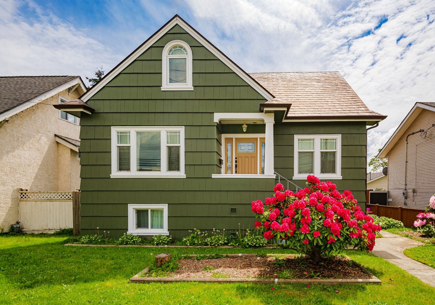 A family bungaloo with green shutters and a yellow-y tan front door.