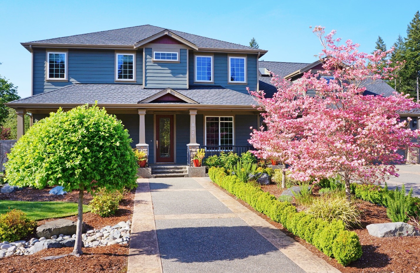A large home with intricate land- and hardscaping. A wide and flat stone walkway leads to the front steps.