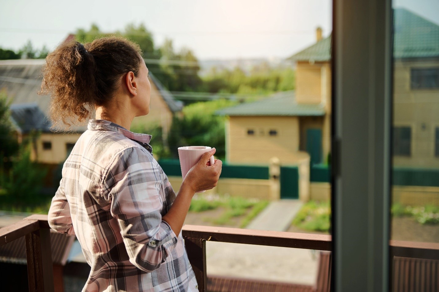 A person looking out on their neighborhood with a cup of coffee from their patio.