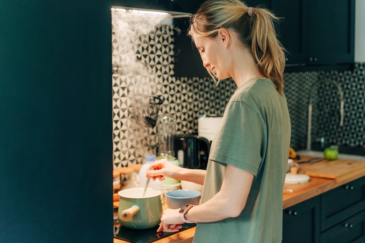 A woman using the stove with steam rising from the pot.