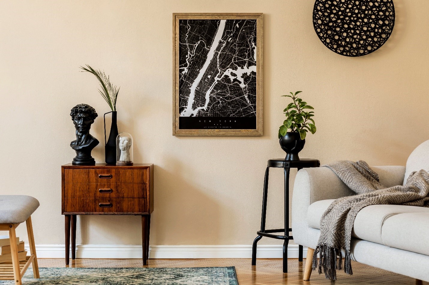 A snippet of a living room. A black and white map of New York neighborhoods hangs in a wooden frame on the wall. A wooden cabinet holds a statue head.