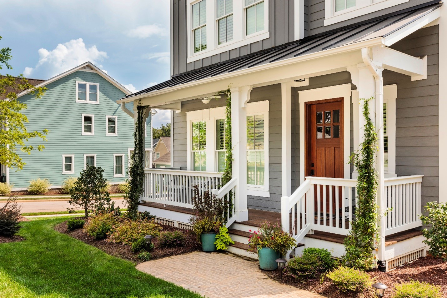 A small front porch with a lot of plants outside and ivy climbing the columns.