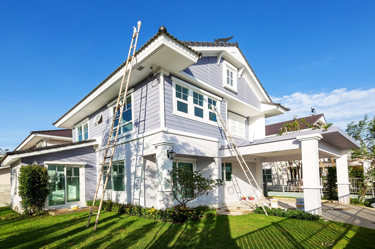 A home with pastel blue siding has ladders leaning against its sides.