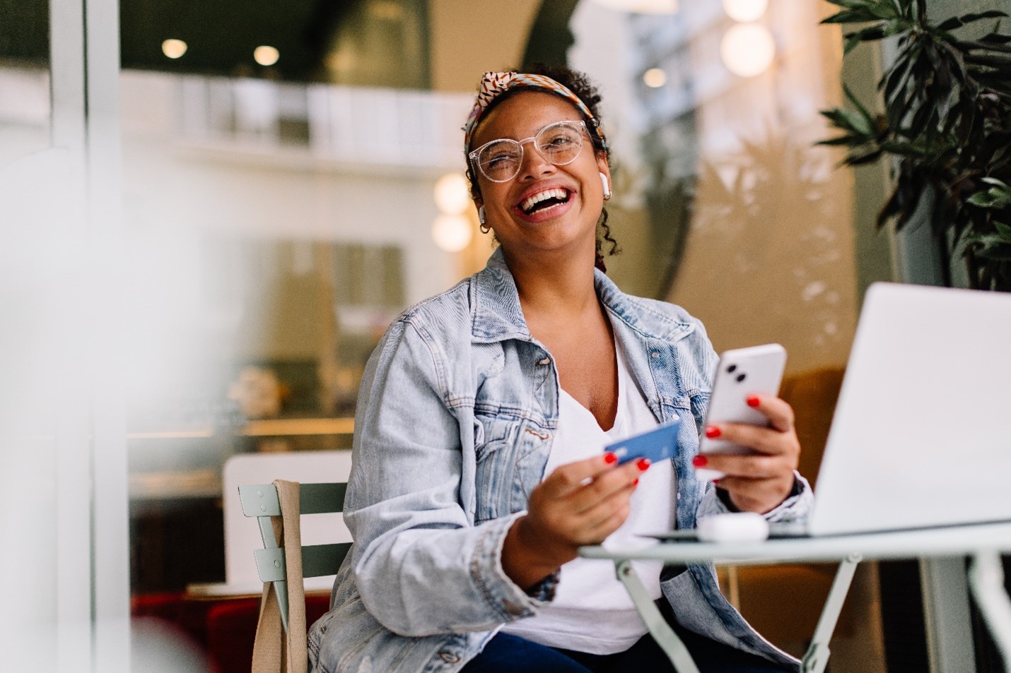 A woman smiling up at someone as she holds her phone in one hand and her credit card in another.