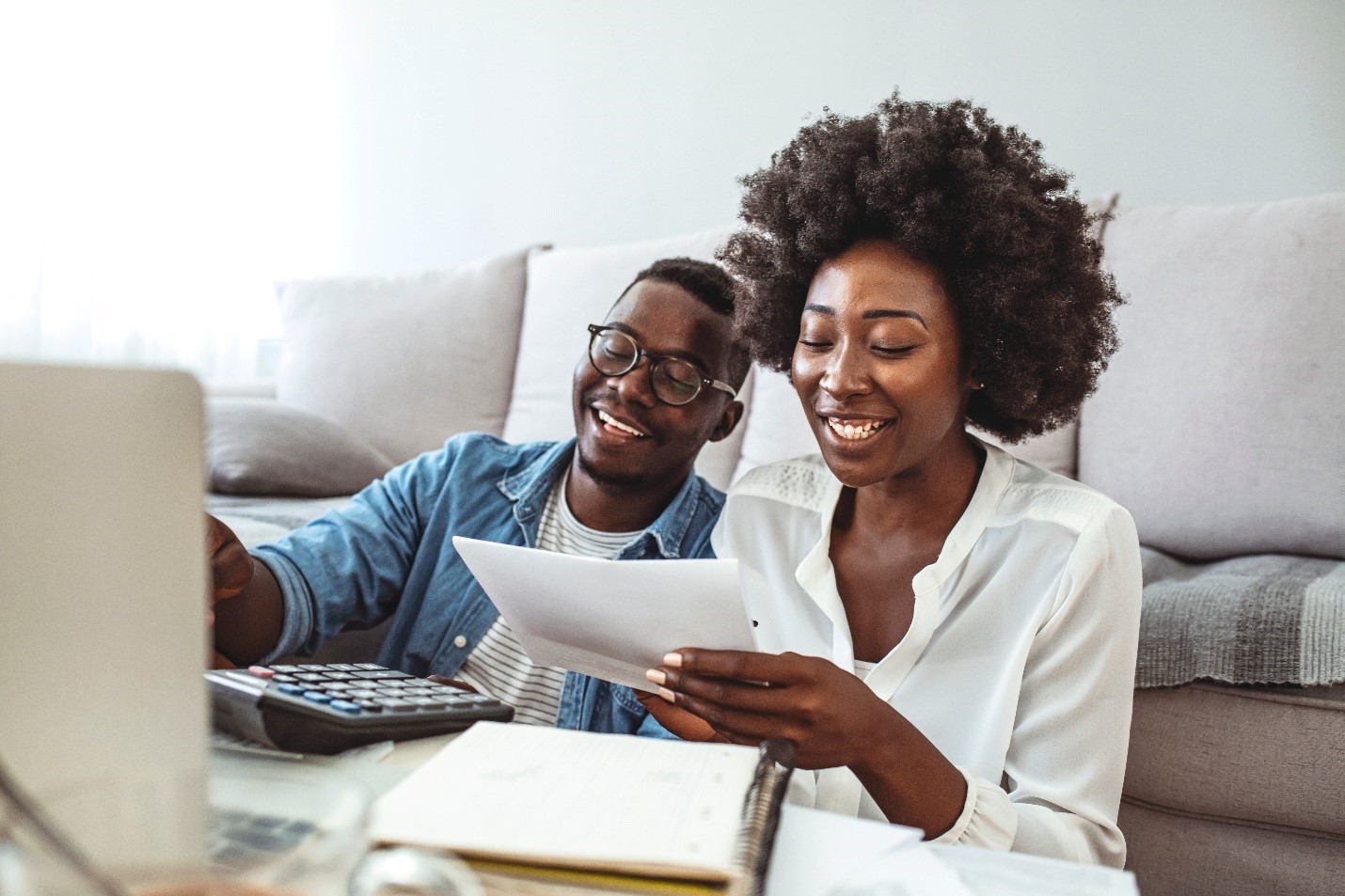 A young black couple laughing together as they look at their finances.