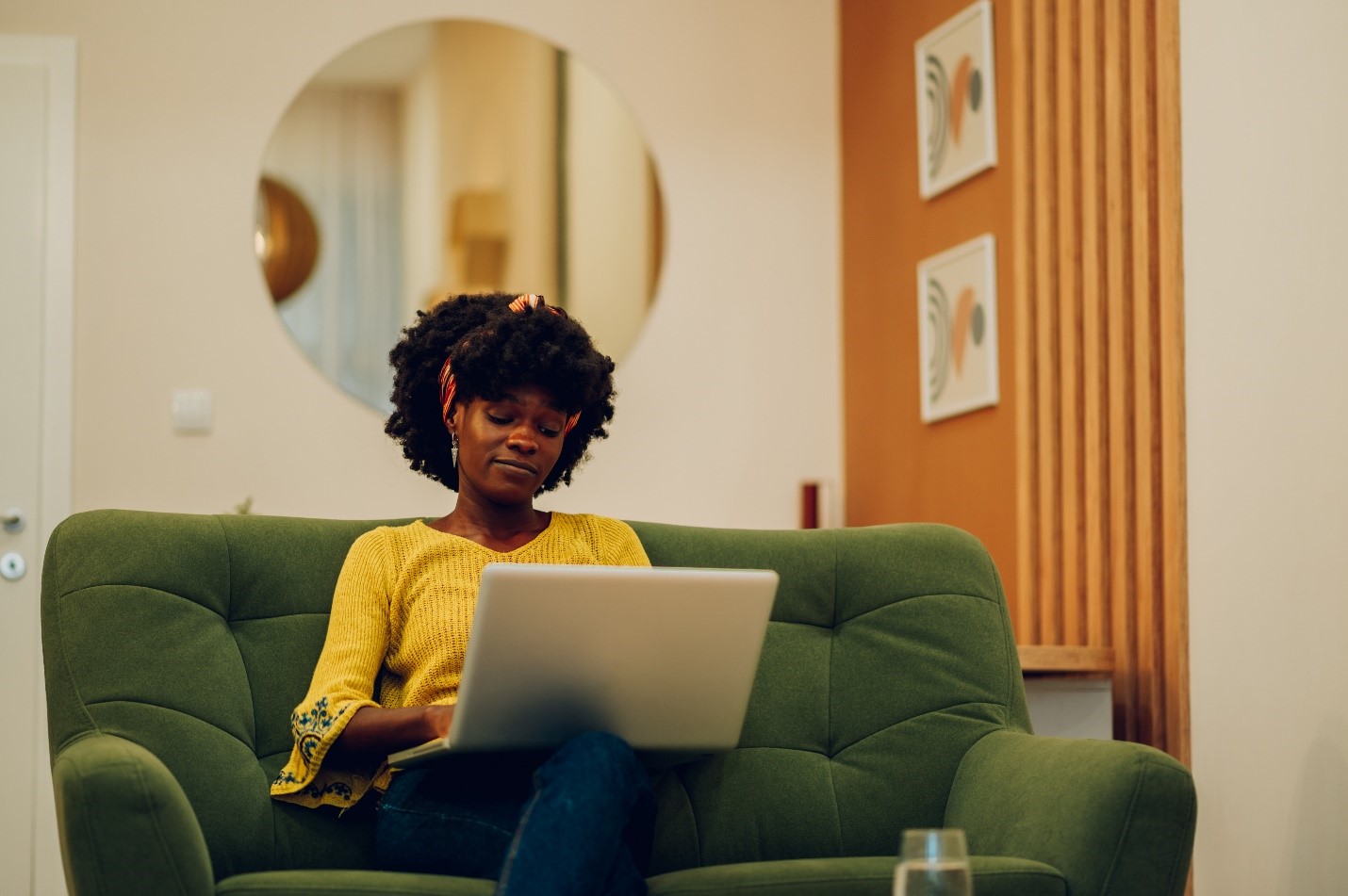 A young woman sits on her green couch, looking contemplative on her laptop.