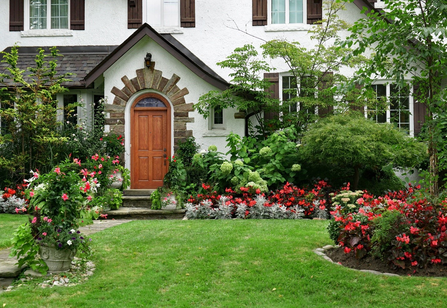 An older cottage home with a decorated front yard with a lot of folliage and flowers.