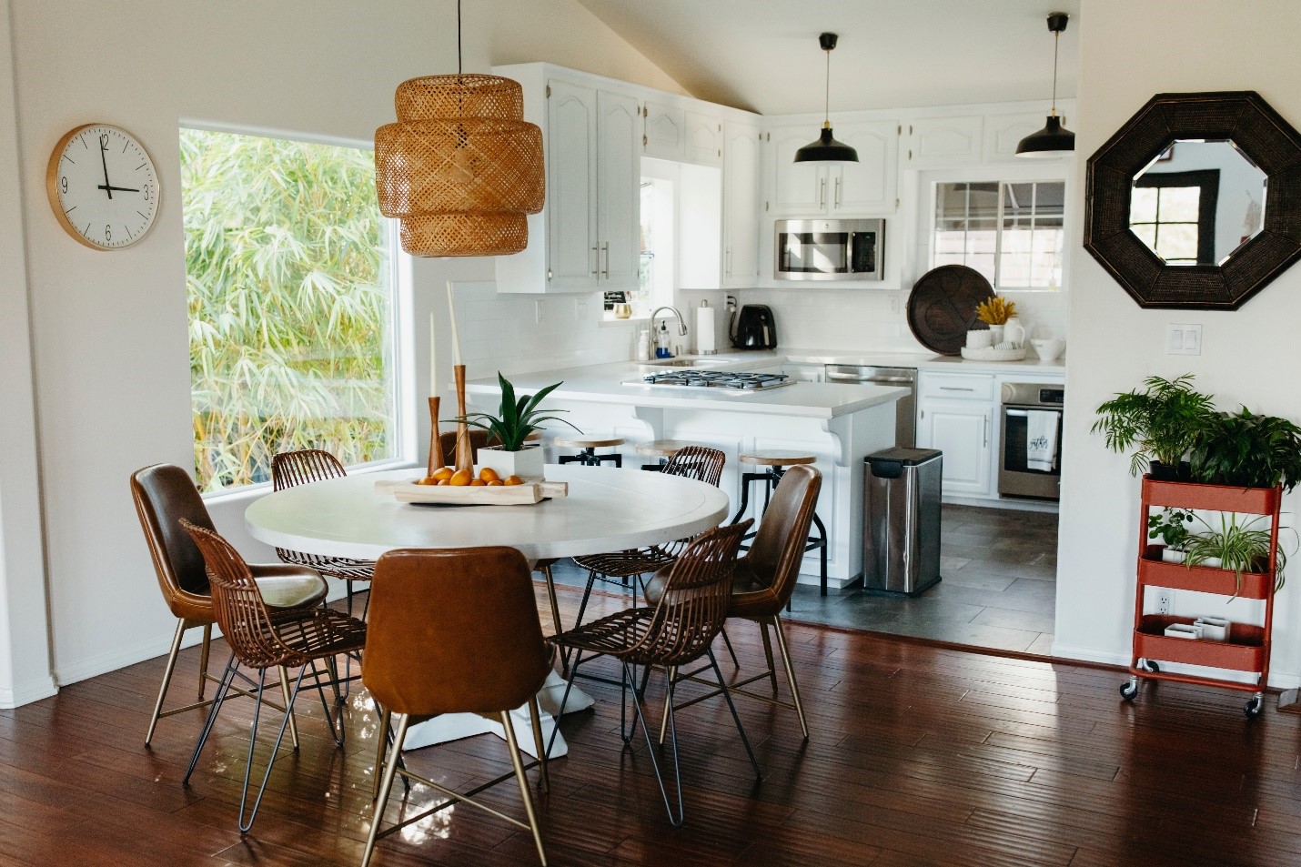 A roomy dining room and kitchen. Light is streaming in through the windows and makes the room appear to be glowing with light. The major surfaces are all white, with dark wood accents.