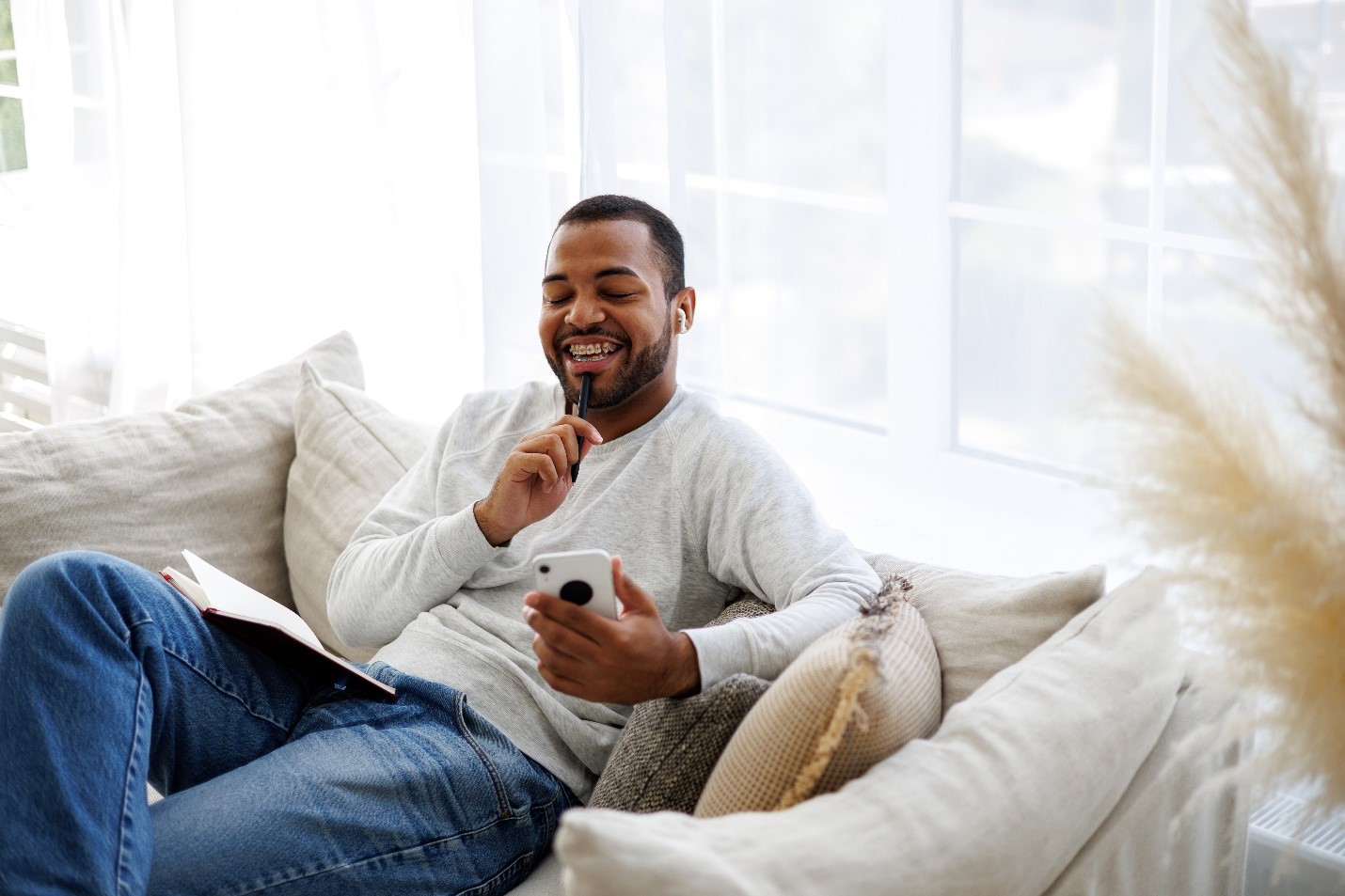 A young man with braces sits on his couch joyfully with his cell phone.
