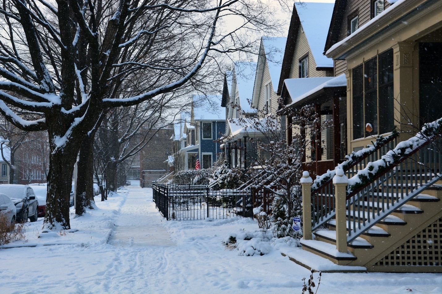 A neighborhood with snow covering the sidewalk.