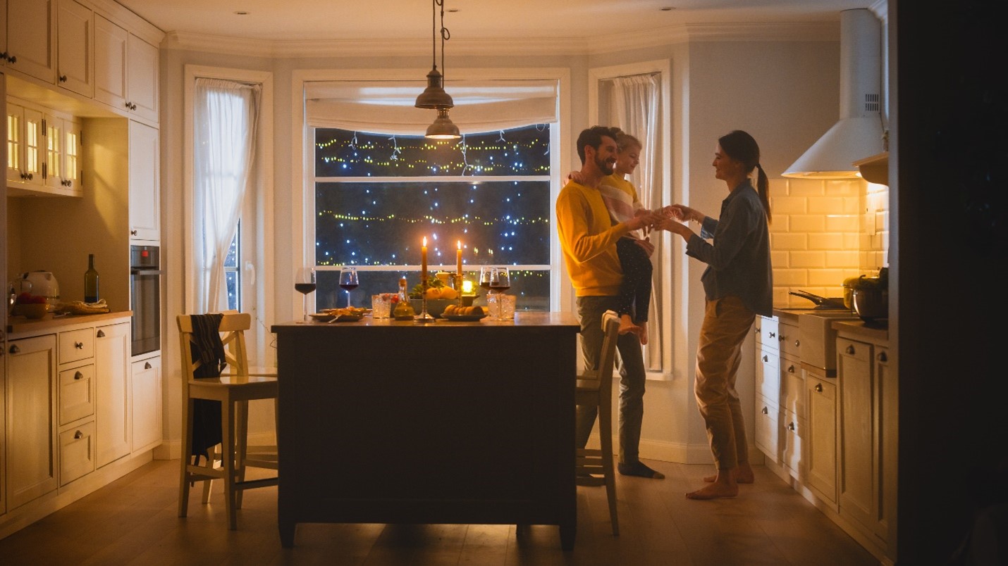 A family cook dinner together. Christmas lights are visible outside.