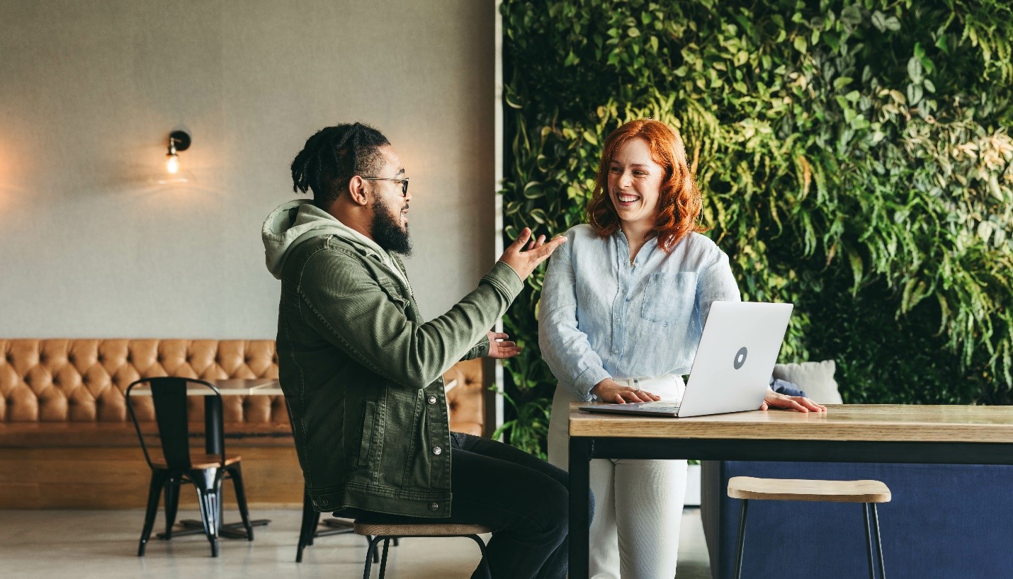 A man chats with a woman in front of a laptop.