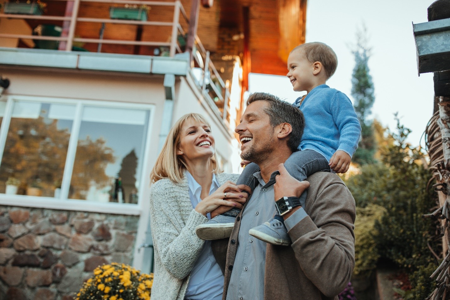 A husband, wife, and baby laughing outside their home.