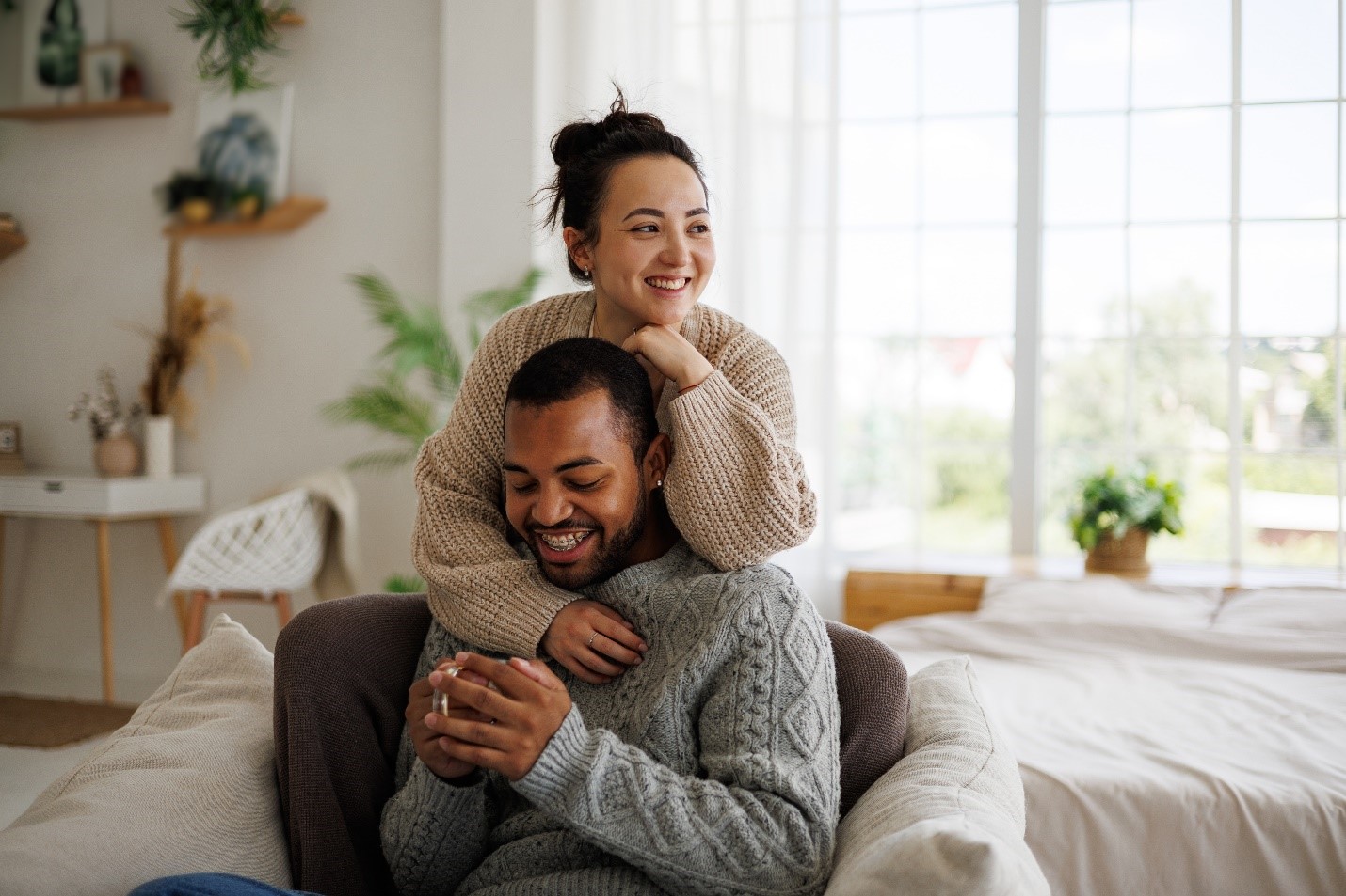 A couple sitting comfortably together at the edge of their bed.