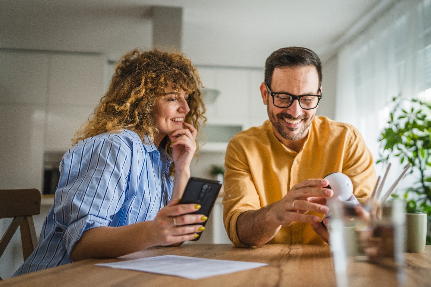 A couple sit at their dining table, inspecting a new security camera and their security app together.