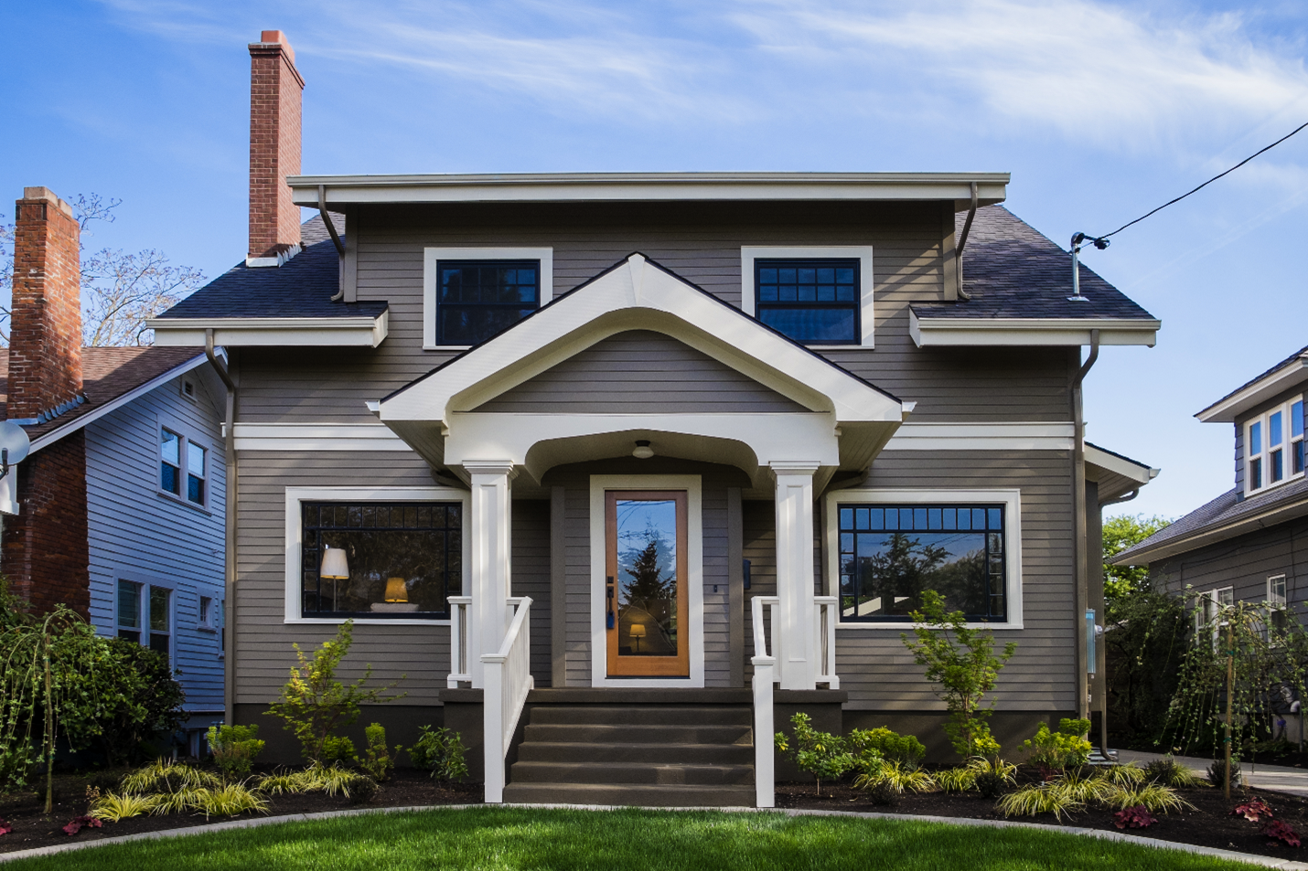 A craftsman style home with gray vinyl siding, a wide entry way to the front door, a low sloping roof covering the upstairs windows, and a wooden front door.
