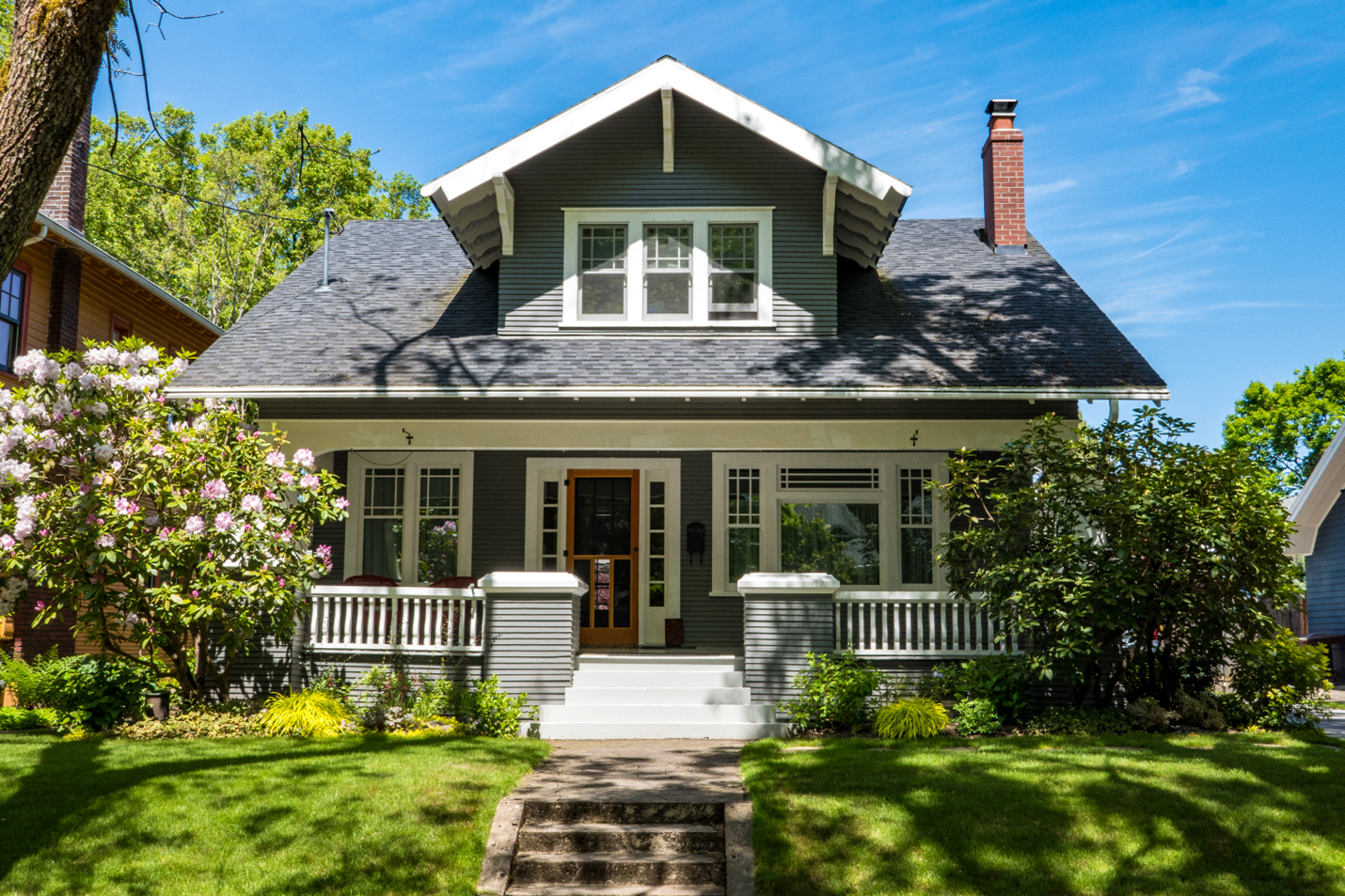 A large bungalow house with green vinyl siding. There is a large front porch that stretches across the length of the home. 