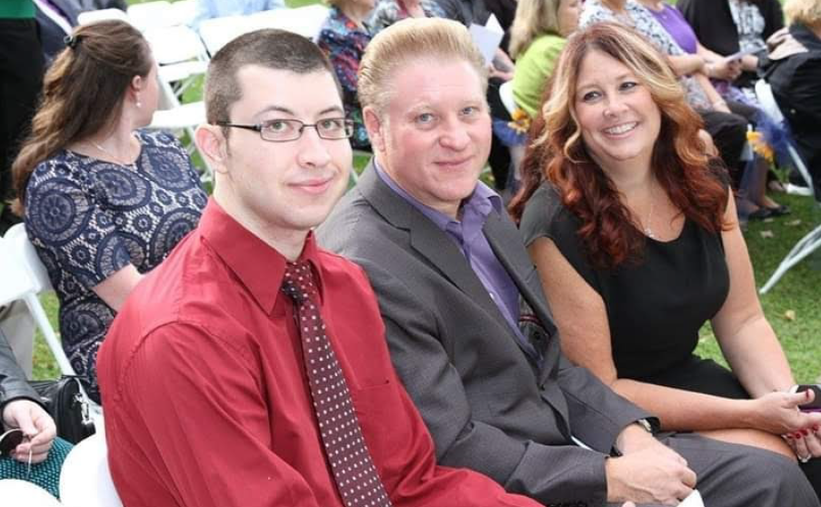 Sherri sits on the right of her husband and son. She is smiling as she looks towards them.